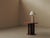 Round pedestal side table featuring a warm reddish-brown wood top and base, contrasted with a dark sculptural central...