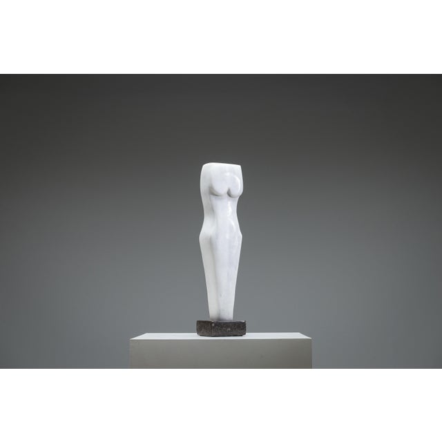 The sculpture stands in quiet authority—an abstract white marble torso, both timeless and deliberately incomplete. Its...