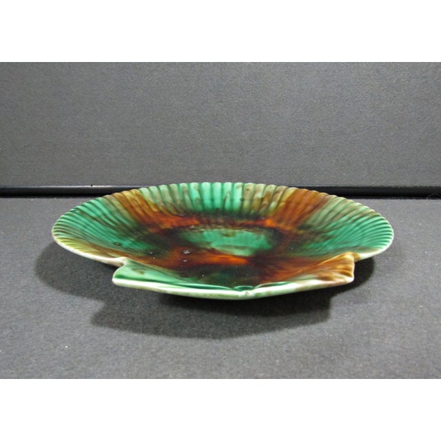 An antique 19th-century Wedgwood majolica scallop-shell shaped plate with mottled green, brown, amber, and cream glaze....