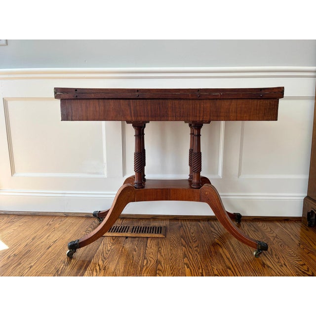 This Duncan Phyfe Style Flip-Top Game Table, circa 1840-1860, features delicate bronze inlay on the apron. The top and...