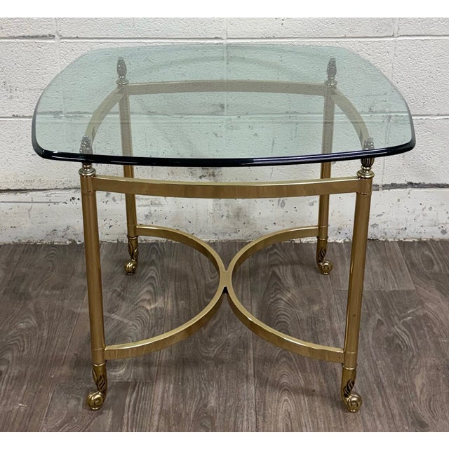 This vintage Hollywood Regency end table features a polished brass frame with elegant urn or flame finials, decorative...