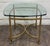 This vintage Hollywood Regency end table features a polished brass frame with elegant urn or flame finials, decorative...