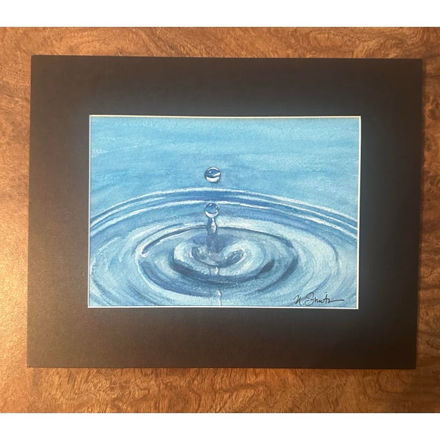 A single suspended water droplet creates expanding ripples in this elegant minimalist watercolor. Layers of luminous blue...