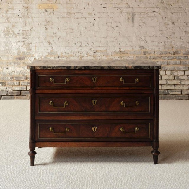 Introduce timeless grandeur to your space with this late 17th century French Empire cherry wood commode with marble top, a...