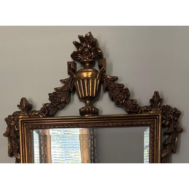 Tall gilt wall mirror in the Baroque / Rococo revival style, with a carved urn-and-floral crest, scrolled side ears,...