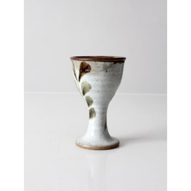 A handmade studio pottery goblet featuring a graceful stemmed form and delicate hand-painted botanical decoration. The...