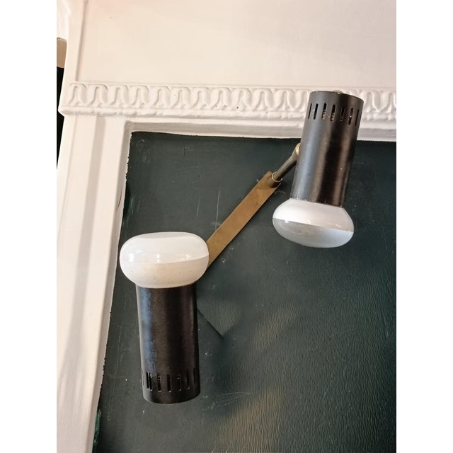 Wall lamp with two adjustable spotlights in black metal, brass frame and joints. The design is minimal and functional: a...