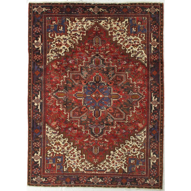 Vintage hand-knotted Persian Heriz wool rug with a red field centered by a large geometric medallion in blue, ivory, and...