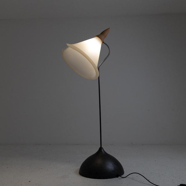 A floor lamp consisting of a hemispherical base and a dark gray painted metal stem. The conical shade is made of white...