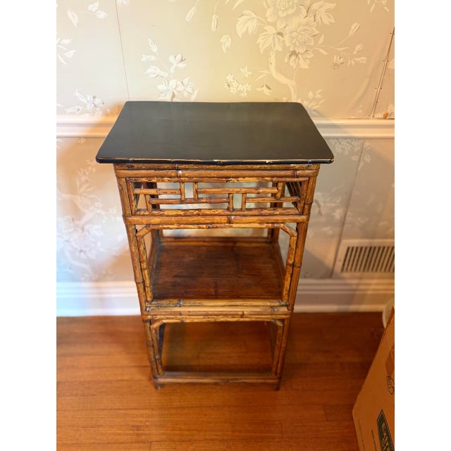 Chinese export bamboo étagère side table in burnt tortoiseshell bamboo with a black lacquered top. An open Chinese...