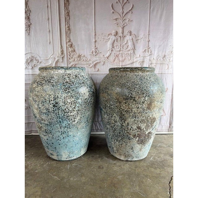 An exceptional pair of oversized rustic terracotta amphora vessels featuring a beautifully weathered surface with organic...