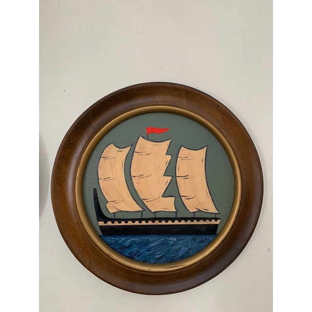 This charming pair of maritime seascapes features black sailing vessels moving across layered blue waters beneath softly...