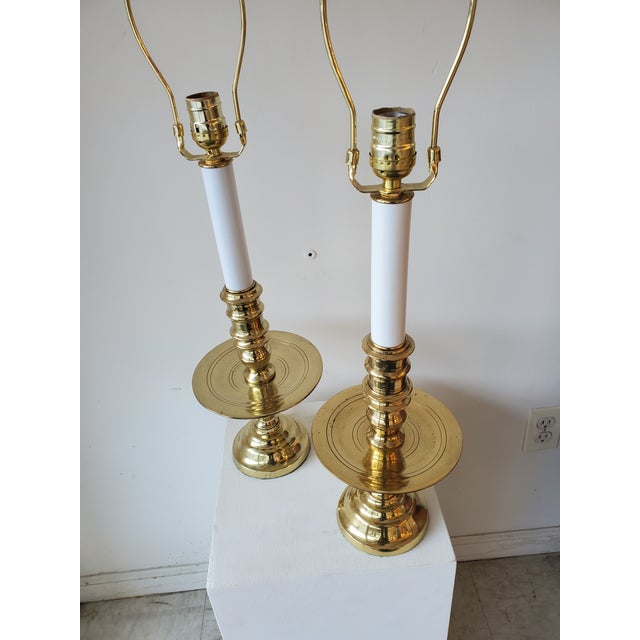 This lamp features a simple design. It has a sturdy brass base with a round, flat plate above the base and a cylindrical...