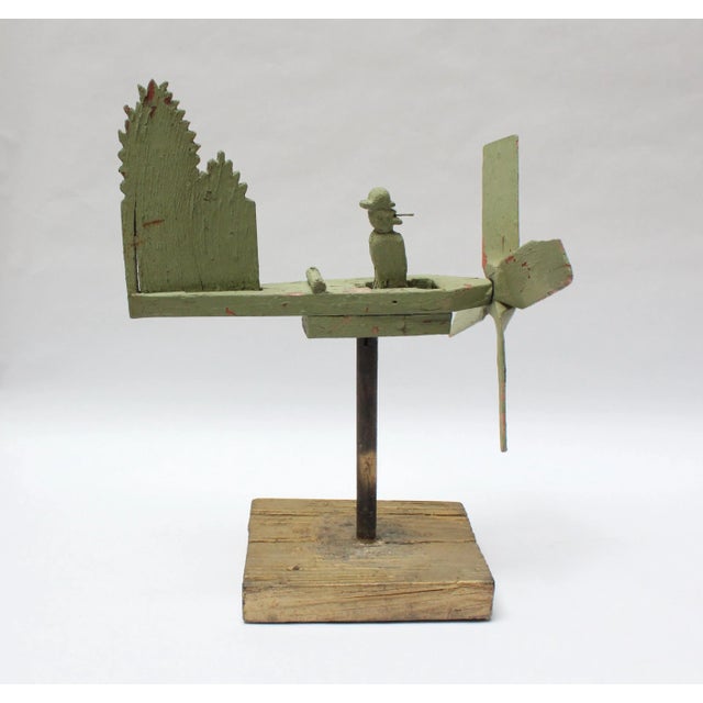 Whimsical avocado green whirligig depicting a man in a canoe / boat smoking a pipe. The green platform has a full 360...
