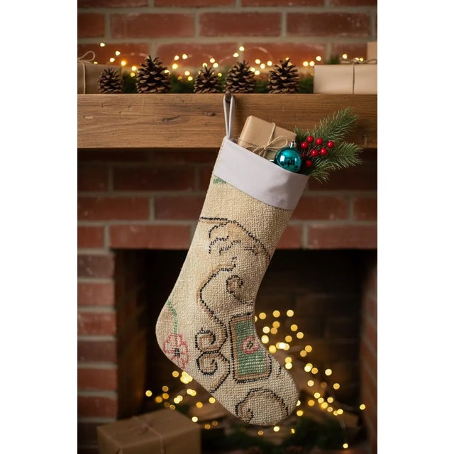 This vintage wool kilim stocking features an elegant golden scrollwork pattern over a soft cream ground, accented with...