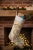 This vintage wool kilim stocking features an elegant golden scrollwork pattern over a soft cream ground, accented with...