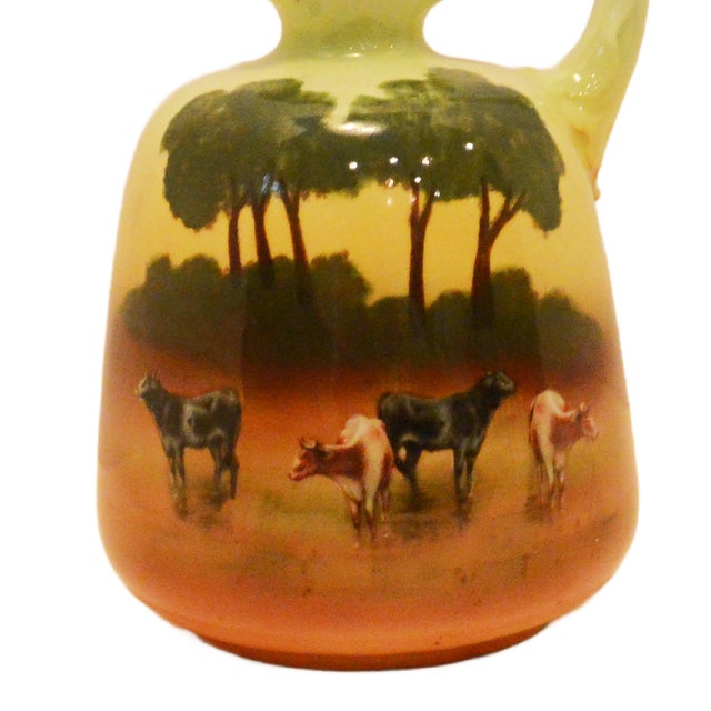 This Royal Bayreuth creamer features the sought-after "Cows in Pasture" scenic motif, rendered in a warm palette of sunset...
