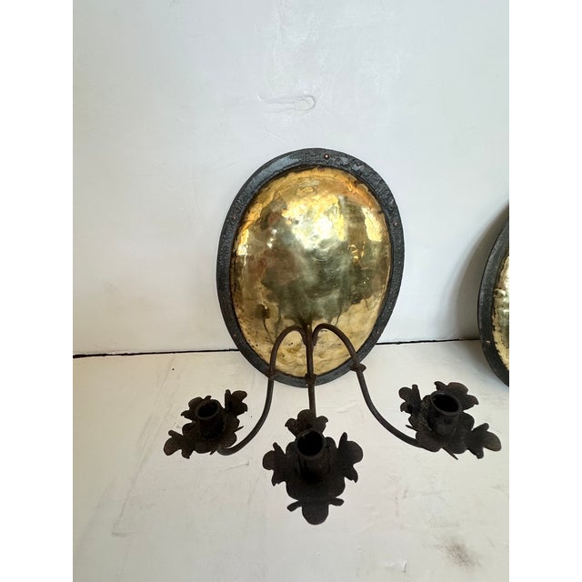Pair of antiqued hand hammered brass and iron candle sconces having oval backs and rustic 3 arm candle holders. SW