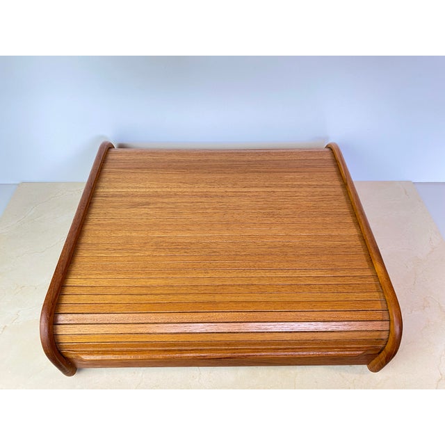 Vintage teak storage box with a rounded, curved-top silhouette and a smooth sliding tambour (roll-top) door with slatted...