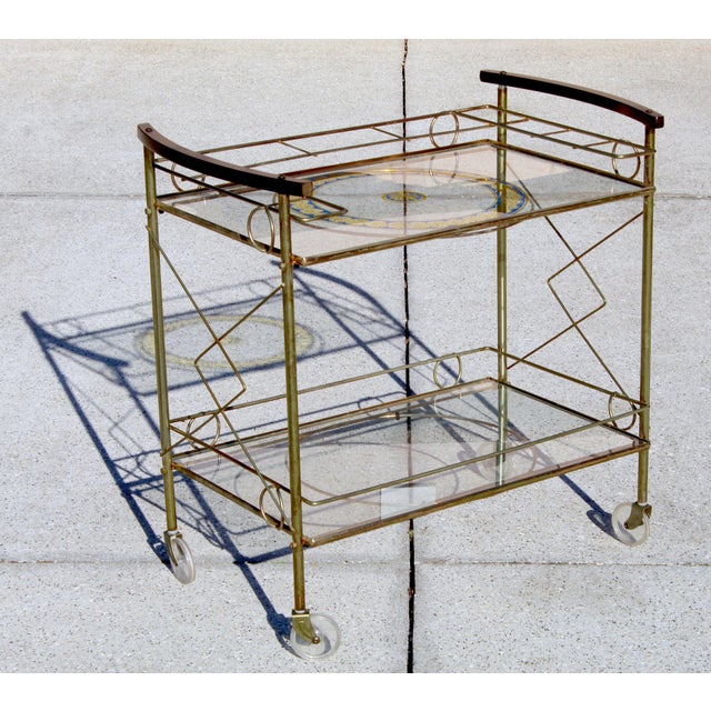 Elegant and eye-catching vintage bar cart featuring a brass frame, two glass shelves, and gracefully curved wooden...