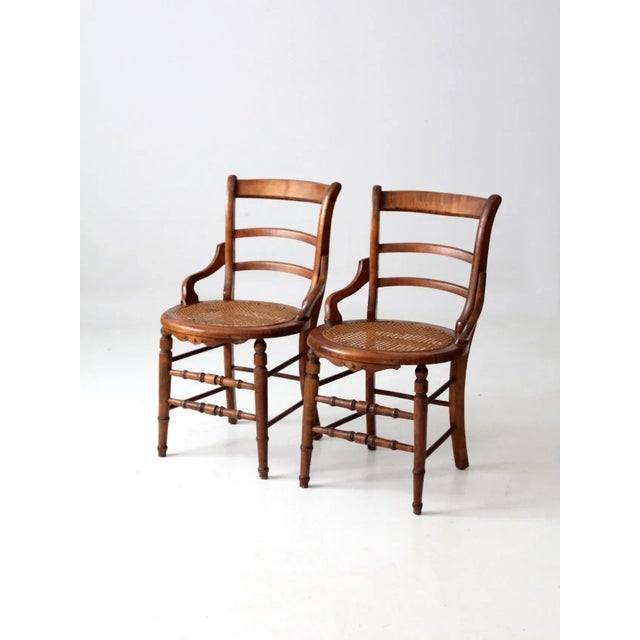 A charming pair of antique Victorian cane-seat chairs, distinguished by their graceful ladder backs, gently arching side...