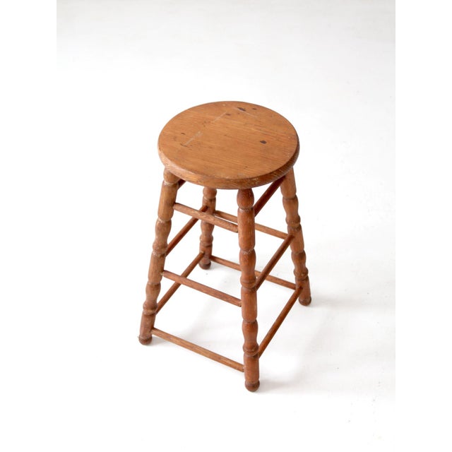 An antique primitive wooden stool featuring a rustic farmhouse silhouette, turned legs, and three tiers of stretchers. The...