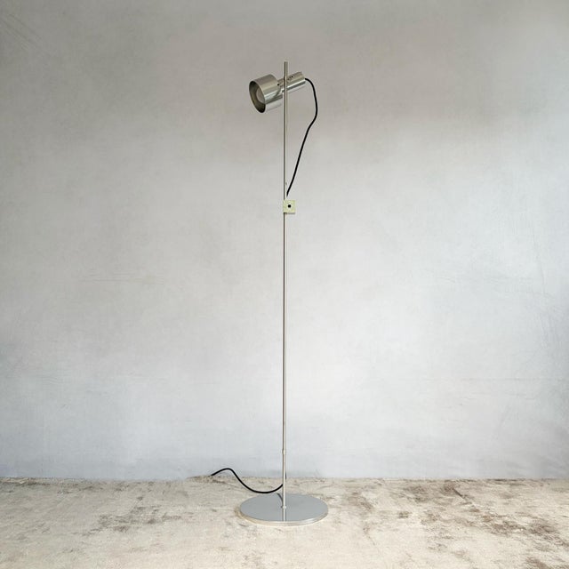 A cylindrical polished aluminium spot head mounted on a slender telescopic steel stem, standing on a weighted circular...