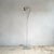 A cylindrical polished aluminium spot head mounted on a slender telescopic steel stem, standing on a weighted circular...