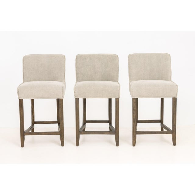 Set of Three Four Hands "Aria" Upholstered Bar Stools, with gray jute and cotton blend upholstery on wooden frames, labels...