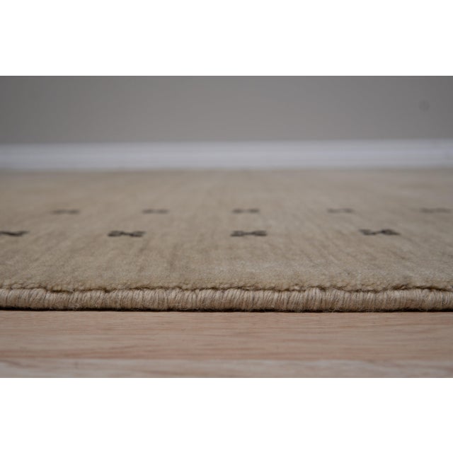 A 5' x 8' hand-knotted wool rug with a plain beige Gabbeh-style field with a simple dotted border in dark brown. Newly...