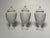 Clean, glossy white porcelain in a neoclassical style adorn this small set of porcelain urns. Each vessel has a lid with...