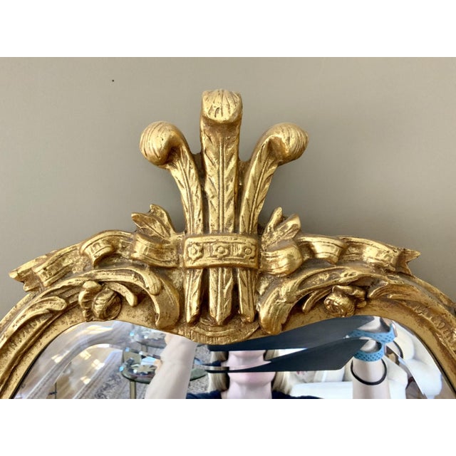 An ornate gilt framed wooden mirror with an elaborate Rococo-style carved Prince of Wales decorative crest and floral...