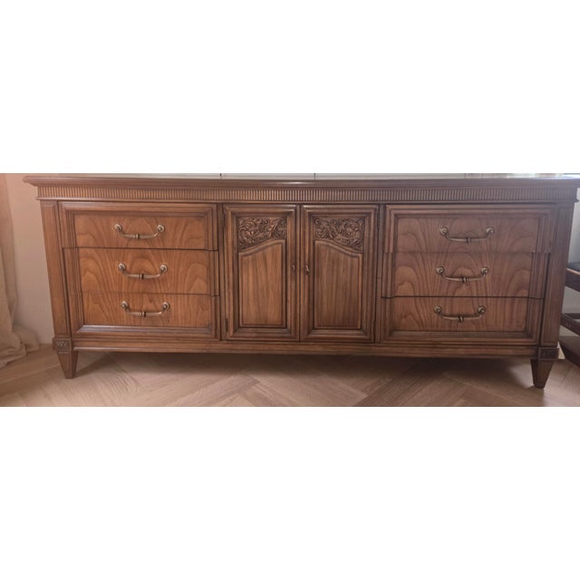 Ornate wooden triple dresser with a medium brown finish. This piece has six drawers with brass-toned swing handles and two...