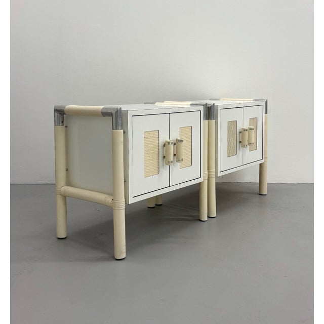 A striking pair of vintage postmodern bedside tables featuring a crisp white lacquered finish accented by faux bamboo...