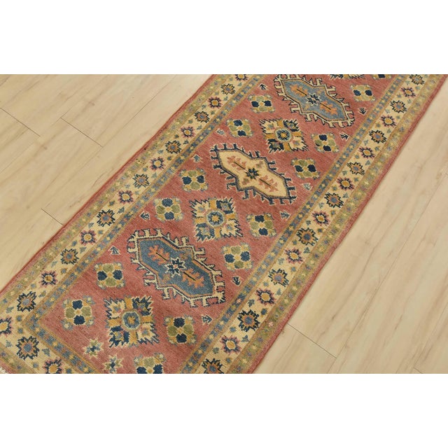 A tribal Caucasian Kazak runner hand-knotted with fine wool on a cotton foundation. This rug features geometric floral...
