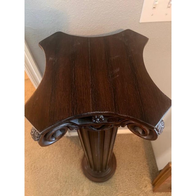 This is a decorative wooden display pedestal featuring classical architectural influences, specifically a column capital...