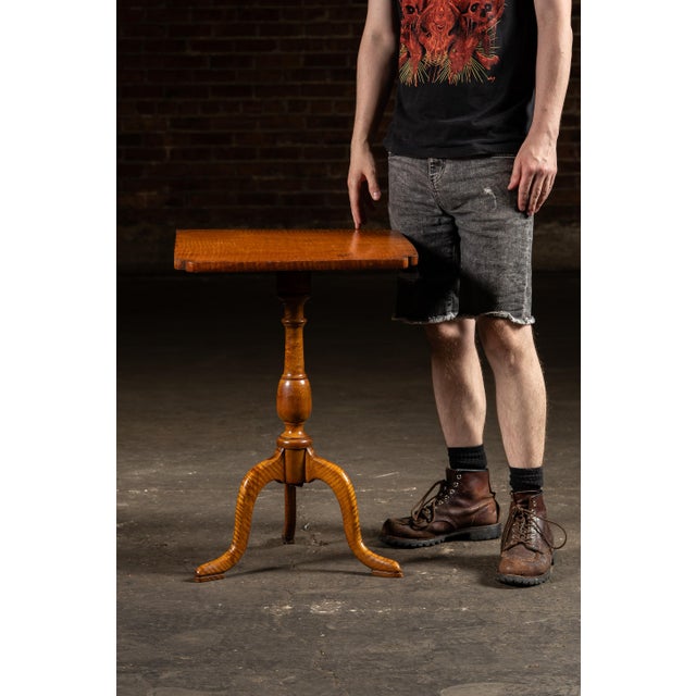 Tilt-top side table in flamed maple with turned column and cabriole tripod base. Crafted from figured maple with a fiery...