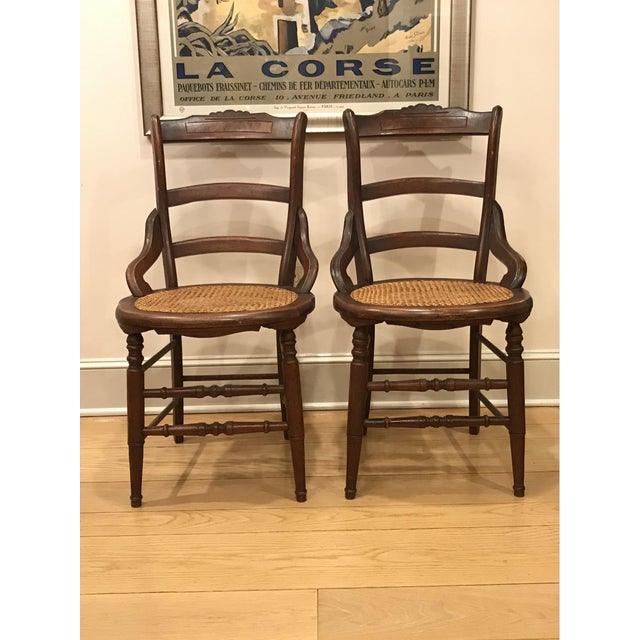 A pair of antique wooden side chairs with cane seats and turned legs and stretchers. Product Information: Materials: Maple...