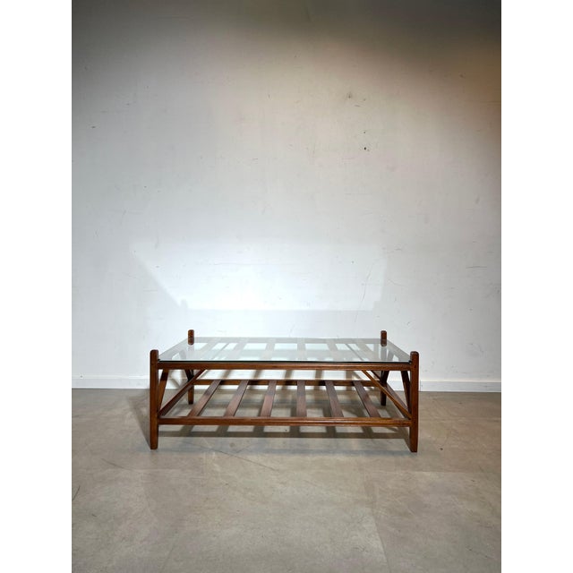 A striking mid-century coffee table featuring a robust wooden frame with a clear glass top. The architectural design of...