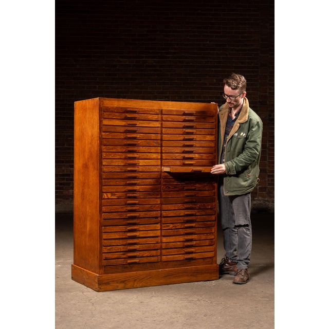 Tall oak index cabinet fitted with forty-eight uniform shallow drawers arranged in a tight grid, designed for systematic...