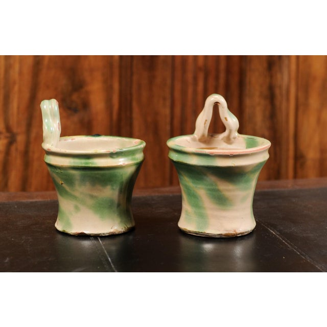 A pair of rustic French pottery hanging planters from the 19th century, with green and yellow glaze. Created in France...
