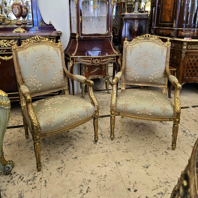 Elegant French-inspired armchair set upholstered in a refined beige damask fabric with a delicate floral motif. The...