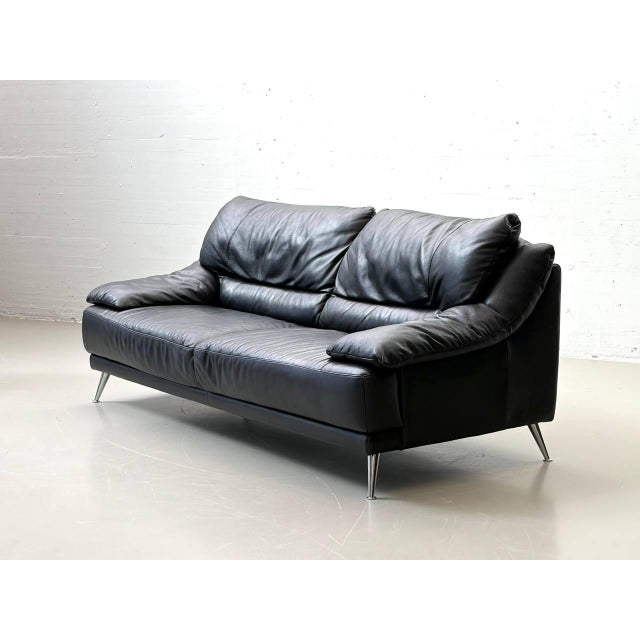 A generously sized three-seater sofa from the italian manufacturer natuzzi, upholstered in high-quality black genuine...