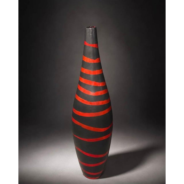 A tall sculptural floor vase with a bold black and red striped finish. The elongated silhouette and graphic stripe pattern...