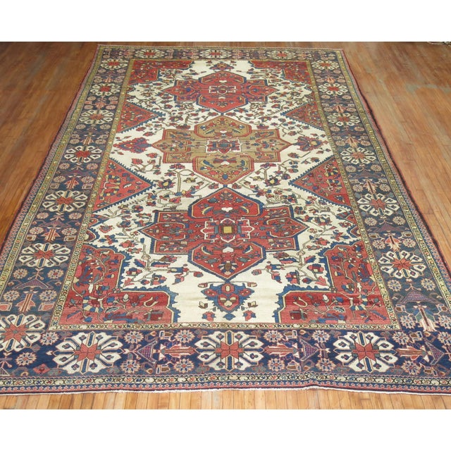 An antique Persian Bakhtiari rug with large scale all-over tribal medallion design on an antique white background....