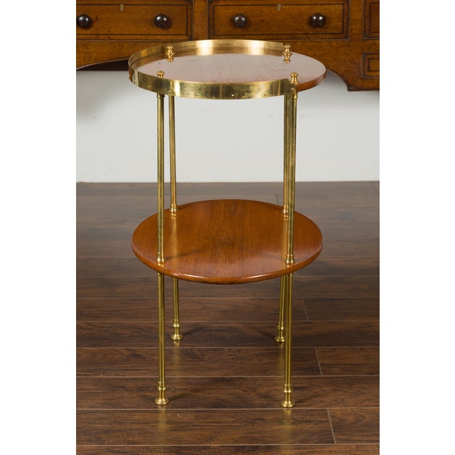 An English mahogany tiered oval table from the mid-20th century, with brass accents. Born in England during the midcentury...