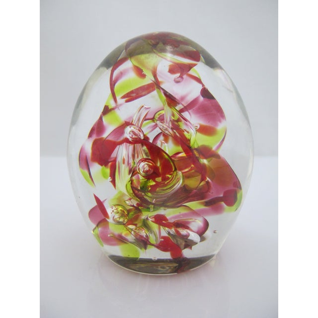 Collectible egg-shaped glass paperweight featuring vibrant swirls of red and yellow suspended in clear blown glass....