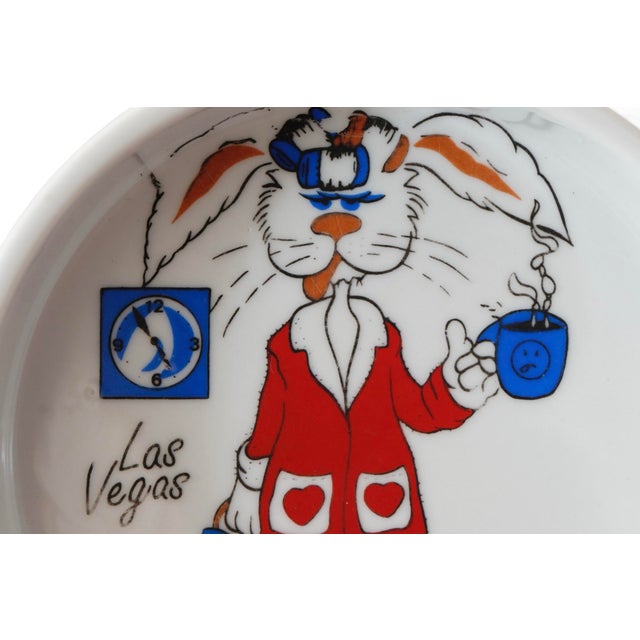 A round souvenir white ceramic ashtray, printed in the center with a rabbit in a dressing gown and slippers, hair dryer...