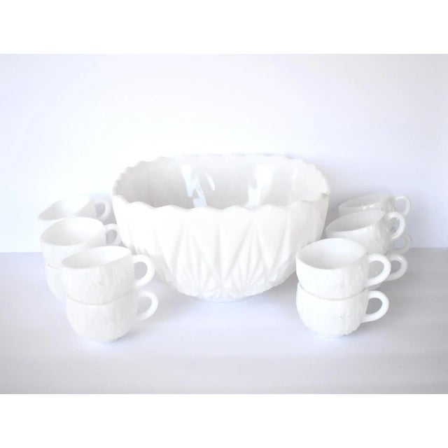 A vintage, mid-century white milk glass punch bowl set with a geometric pressed glass design and a rounded, squarish...