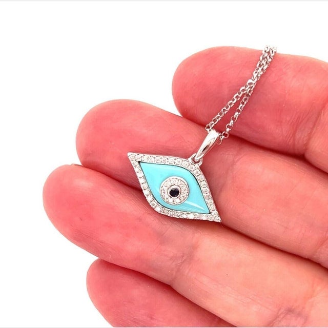 This Diamond Turquoise Sapphire 18k White Gold Evil Eye Pendant Necklace is a stunning piece of fine jewelry. The pendant...